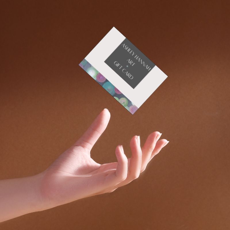 Hand reaching out towards a gift card with 'Ashley Hannah Art' on a brown background